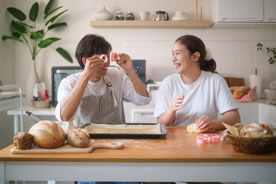 Cheerful couple laughing while baking cookies together in a bright home kitchen.