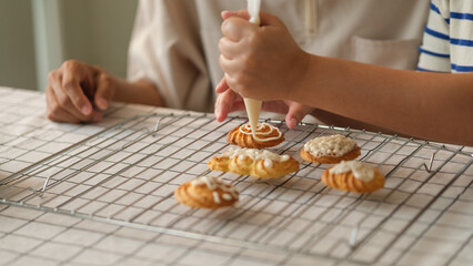 Close up of couple decorating cookies with icing on a cooling rack in a home kitchen.