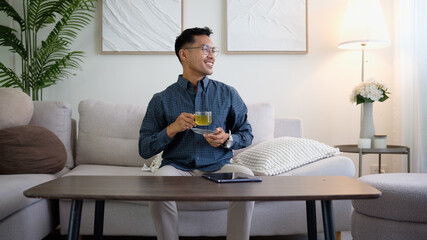 Smiling man sitting on a sofa enjoying a cup of green tea in a cozy living room.