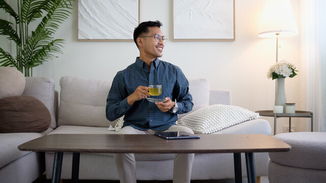 Smiling man sitting on a sofa enjoying a cup of green tea in a cozy living room.
