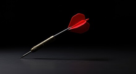 A single red dart with a metallic body and sharp point lies diagonally on a dark surface.
