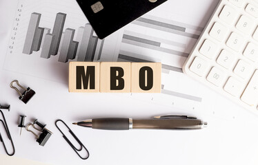 MBO acronym on wooden blocks with financial documents, pen, credit card, and calculator on desk