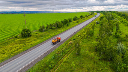trucks drive along the road in the summer, surrounded by green fields