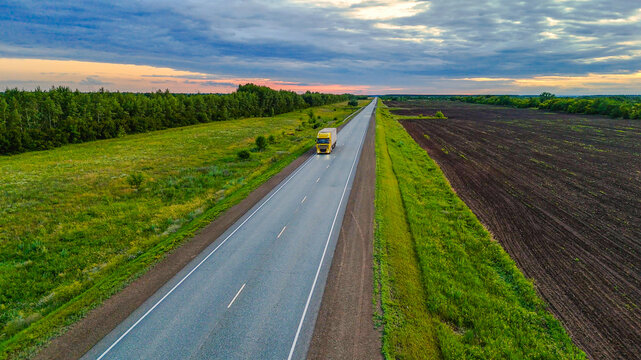 trucks drive along the road in the summer, surrounded by green fields