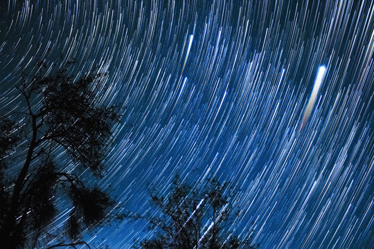Milky way stars trails with rural countryside silhouettes.