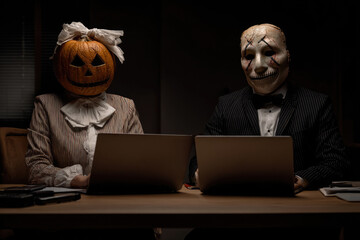 employees in funny masks and Halloween pumpkin on head working on laptops in office.