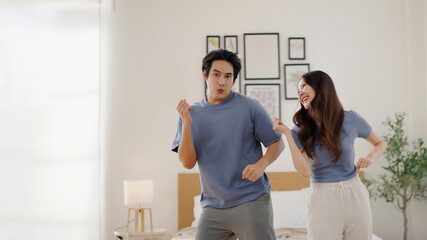 Fototapeta premium Happy Asian man and woman enjoying a fun moment dancing together at home in casual clothes