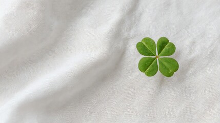 A fresh green four-leaf clover lays on a textured white fabric background, symbolizing luck and hope.