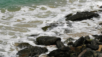 Fototapeta premium The foam of sea waves crashes on the rocks at Dhanushkodi beach in Tamil Nadu, India