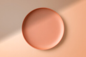 Fototapeta premium Minimalist top-down view of an empty ceramic plate on a pastel beige and peach background with a soft shadow. Ideal for product mockups.
