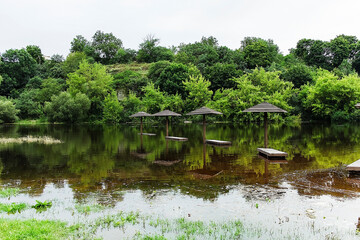 Wooden parasols stand submerged in a flooded river, their reflections shimmering beneath the golden light of summer.