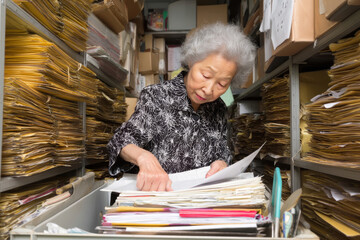 Elderly Asian woman curating an archive of company publications, scanning and indexing newsletters