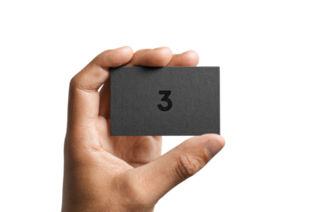 A hand holds a dark gray business card.  The card has a simple, bold number "3" printed on it