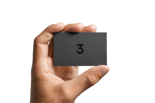 A hand holds a dark gray business card.  The card has a simple, bold number "3" printed on it