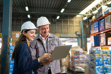Warehouse Manager  and supervisor in inventory data on a laptop amid stacked pallets.