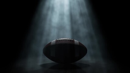 A generic american football sports ball being lit by a single rotating and swirling ethereal light ray on a dark black background