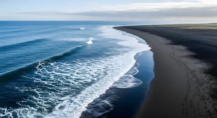 Dark sand beach meets ocean waves under a partly cloudy sky.  Whitecaps form as waves break on the shore.