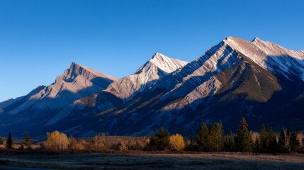 Fototapeta premium Majestic rocky mountains at sunrise with snow-capped peaks and autumn forest