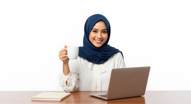 A smiling Muslim woman in a blue hijab holds a white mug while working at her desk with a laptop.