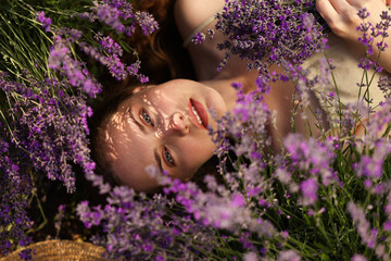 Beautiful young woman lying among lavender flowers outdoors, top view