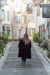 Vertical image of a woman strolling through the picturesque village of Salies-de-Béarn in southern France, taking in the charm of its vibrant, colorful façades and quaint architecture