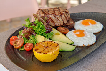 A Delicious Plate Featuring Grilled Steak, Fresh Vegetables, Poached Eggs, and Charred Citrus on a Stylish Black Platter for a Gourmet Experience