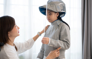 Obraz premium A girl in fencing gear with their mother preparing sports equipment