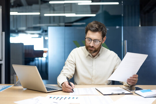 A serious and focused young man is sitting at a desk in the office, working and writing documents