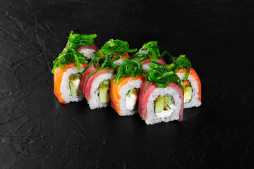 Sushi rolls covered with wakame seaweed and salmon, tuna and avocado on black background