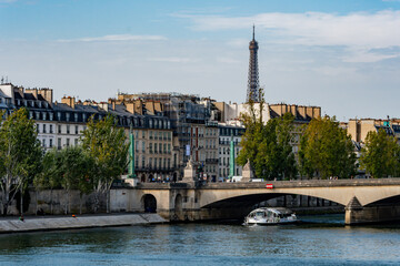 A tour boat on the Seine River, passing a bridge with the Eiffel Tower visible on the horizon.