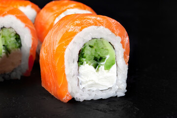 Philadelphia uramaki sushi rolls with salmon, cream cheese and cucumber filling on dark background