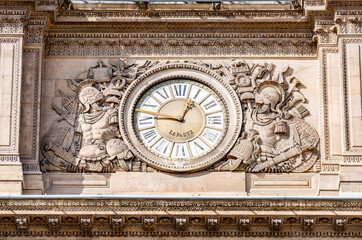 Close-up of an ornamental clock on the Louvre Palace facade, surrounded by intricate sculptures.