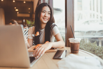 Fototapeta premium Happy smile asian woman eating croissants at cafe sitting near window indoors on day