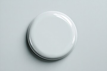 A top-down view of a smooth, blank, white, round object.  It appears glossy,  with subtle highlights.  Placed on a neutral light-gray surface
