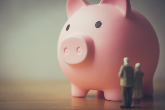 Senior couple and pink piggy bank on wooden table with white wall background. Money financial management, pension, savings planning, deposit account for elder or retirees, aging society, ira concept.