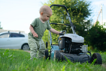 Fototapeta premium Little child in nature exploring garden lawnmower with innocent curiosity. Safe outdoor environment concept for kids and proper lawn maintenance.
