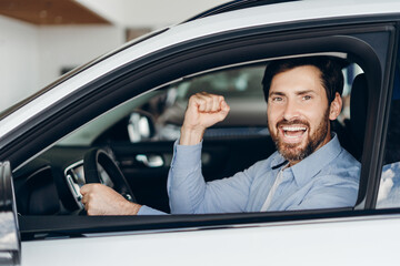 Happy businessman celebrating success inside new car at dealership