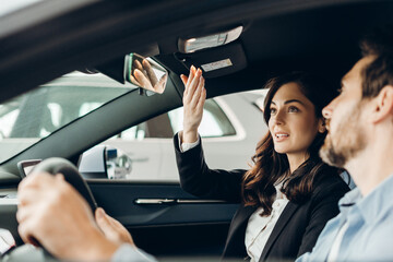 Car saleswoman adjusting rearview mirror for customer in dealership