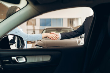 Woman and car salesman shaking hands at dealership