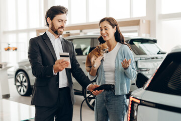 Obraz premium Salesman showing credit card reader to woman charging electric car with dog