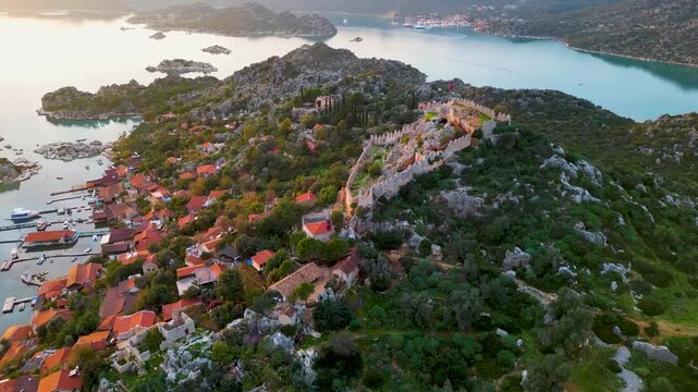 Aerial view of the Castle of Simena and the coastal village on the Mediterranean Sea, Antalya Province, Turkey. Calm sea, ancient ruins, and sunset light over the island and fortress.