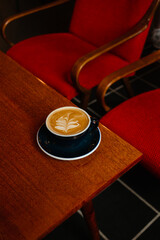 Cappuccino with plant based milk in a large mug on a wooden table. A cup of coffee against the background of cozy red armchairs. Specialty coffee concept