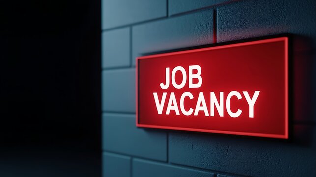 A glowing red sign reading "JOB VACANCY" is illuminated against a dark wall, suggesting available employment opportunities.