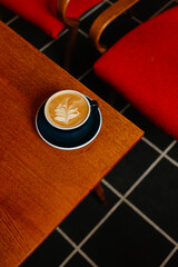 Flat white in a large cup on a wooden table next to red armchairs. Coffee break in a special coffee shop. Aromatic coffee with milk for breakfast