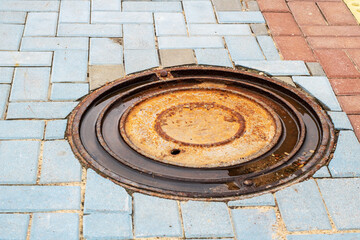 A worn and rusty manhole cover sitting on a brick sidewalk