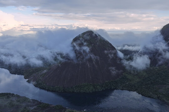 Aerial view of the majestic Cerro Mono, shrouded in ethereal clouds, rises dramatically from the dark, mirror-like waters, Inirida, Guainia, Colombia.