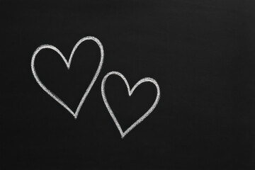 Two hand drawn chalk hearts sketched on clean blackboard background, symbolizing love and romance, with space for text