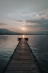 Fototapeta premium Wooden pier extending into tranquil water at sunset.