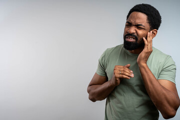 Black man suffering from ear pain and tinnitus, touching ear in discomfort, possible infection,...