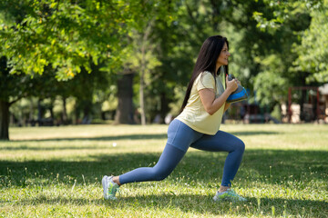 Fit smiling woman doing kettlebell lunge exercise in park during morning strength workout for body shaping	